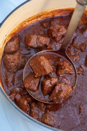 A ladle scoops up chunks of beef from a Dutch oven.