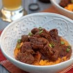 A white bowl with mashed sweet potatoes topped with pieces of beef.