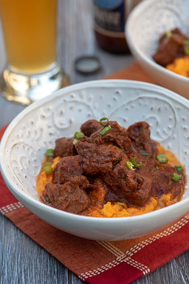 A white bowl with mashed sweet potatoes topped with pieces of beef.