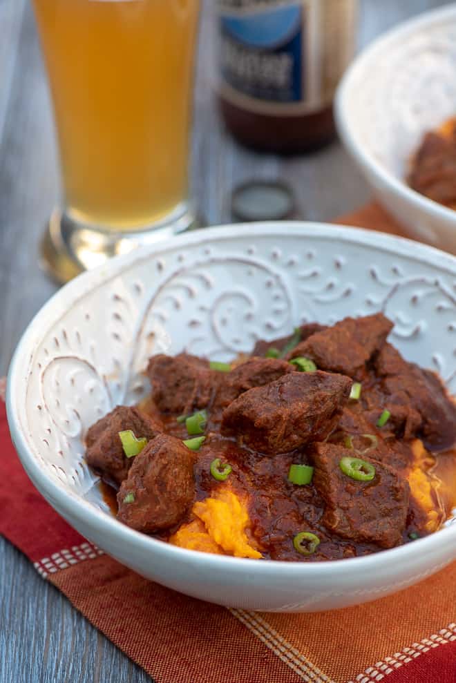 A serving of Smoky Chili Braised Beef over a mound of mashed sweet potatoes in a white bowl.
