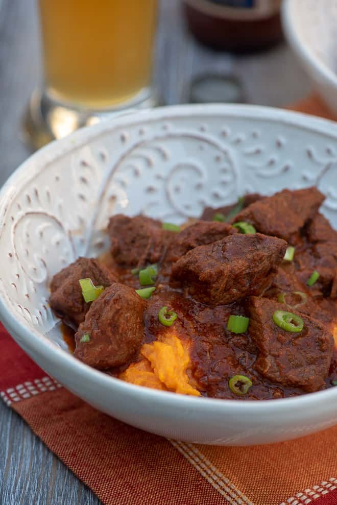 A close up shot of the beef over a mound of mashed sweet potatoes in a white bowl.