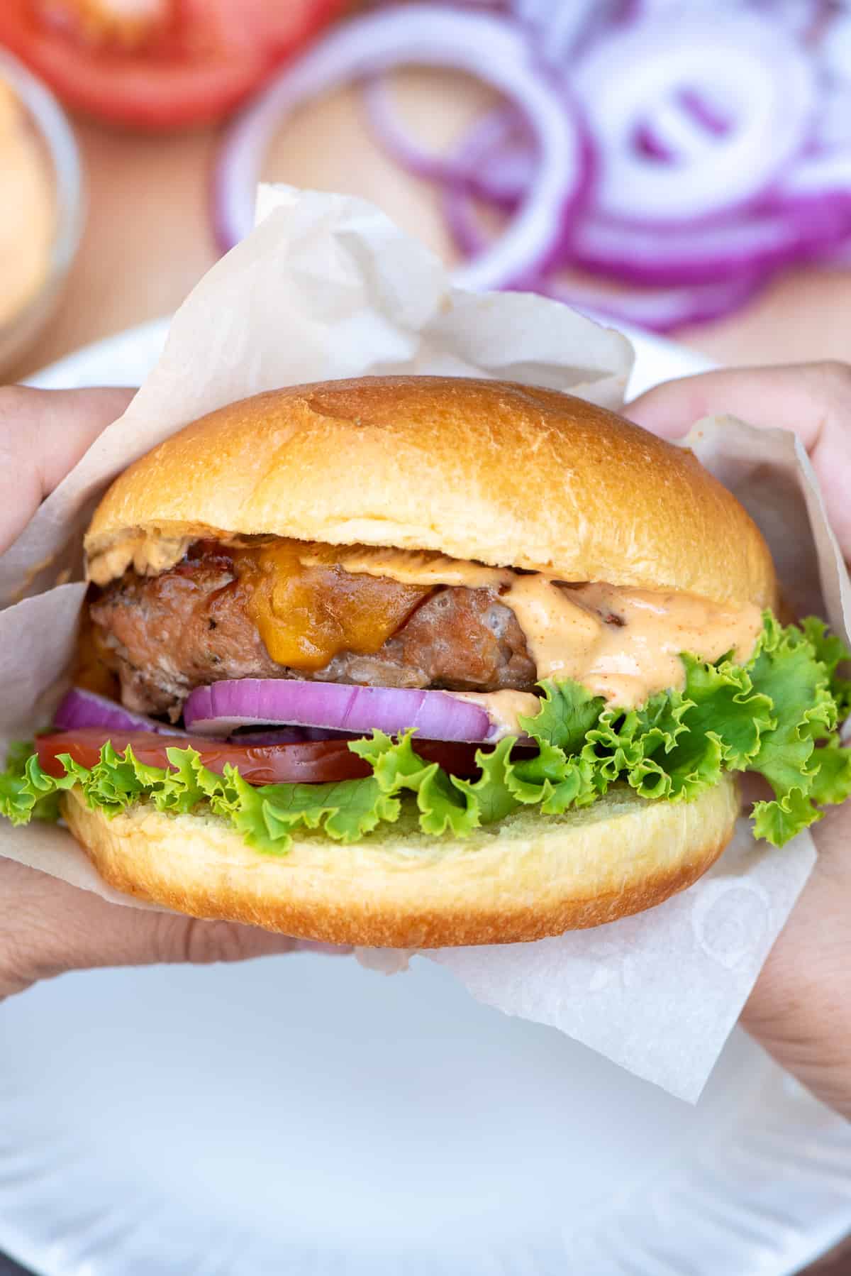 Hands hold a turkey burger with sauce oozing out the front.