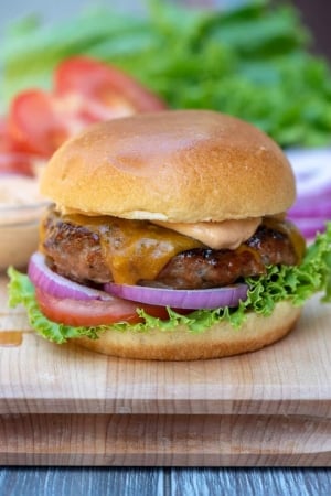 A close up of a turkey burger sitting on top of a wooden cutting board.