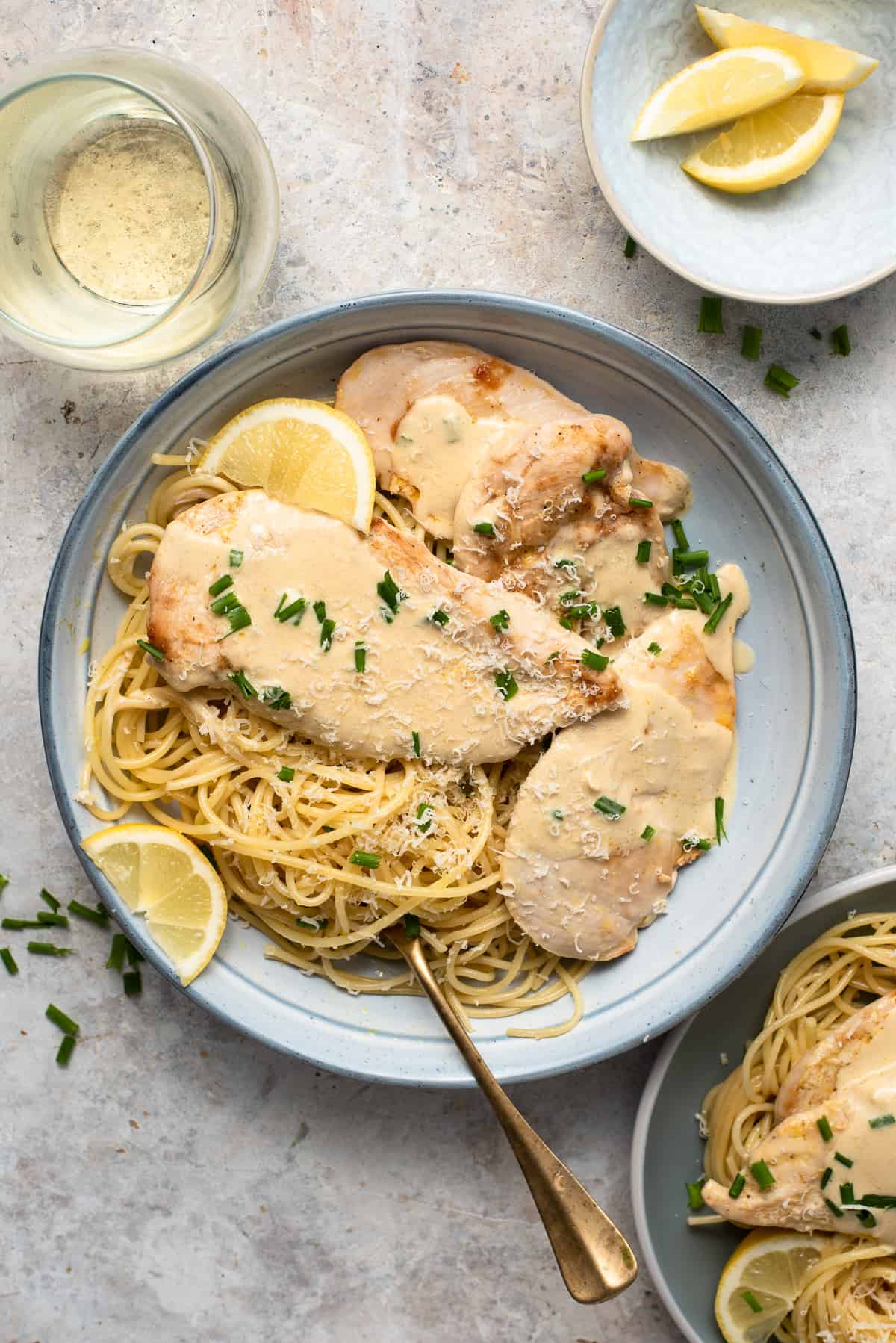 A top down shot of chicken scallopini on a plate with parmesan noodles and lemon wedges.