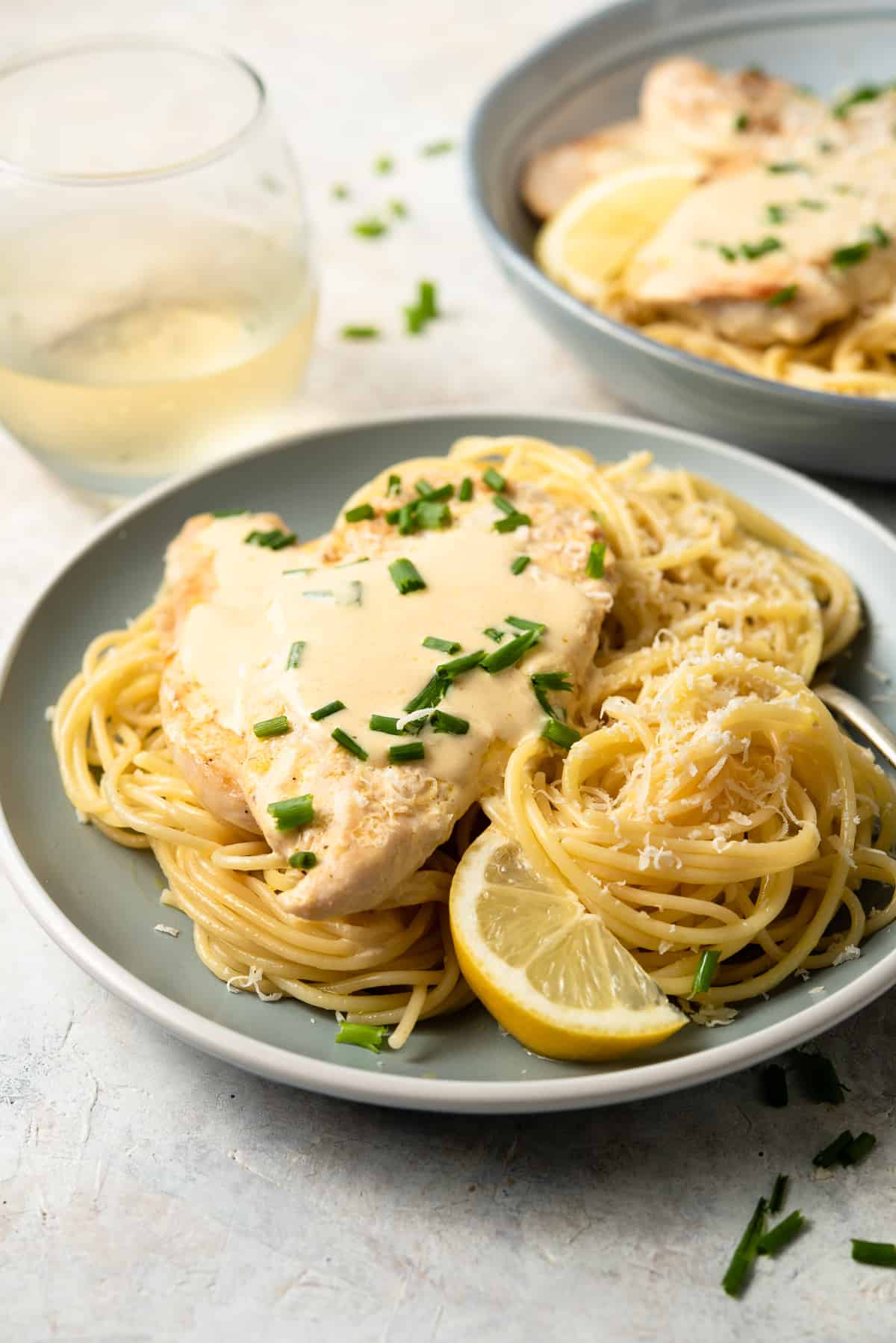 Chicken Scallopini with Parmesan noodles on a plate with lemon wedges.