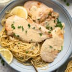 A top down shot of chicken scallopini on a plate with parmesan noodles and lemon wedges.