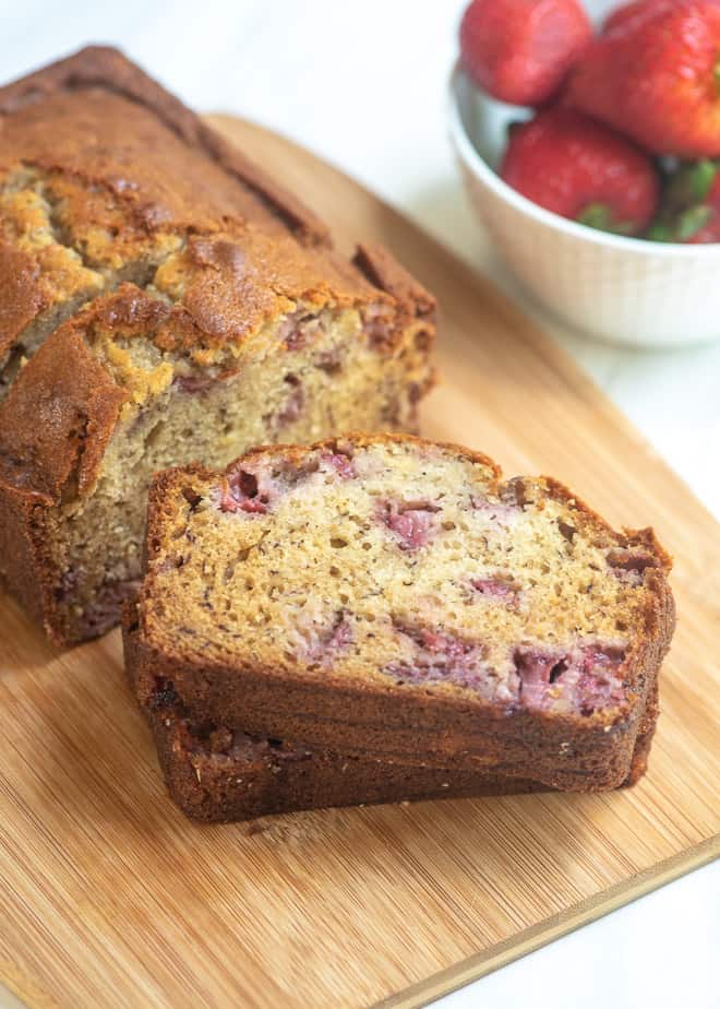 A loaf of Strawberry Banana Bread on a cutting board with two slices stacked on top of each other in front of it.