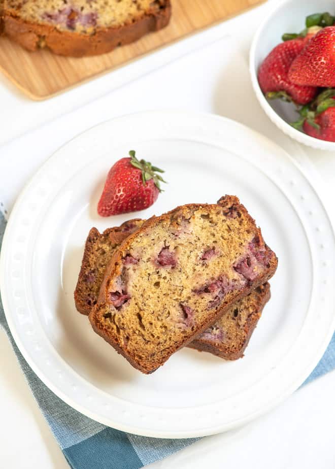 Two slices of Strawberry Banana Bread on a white plate with a fresh strawberry next to it.