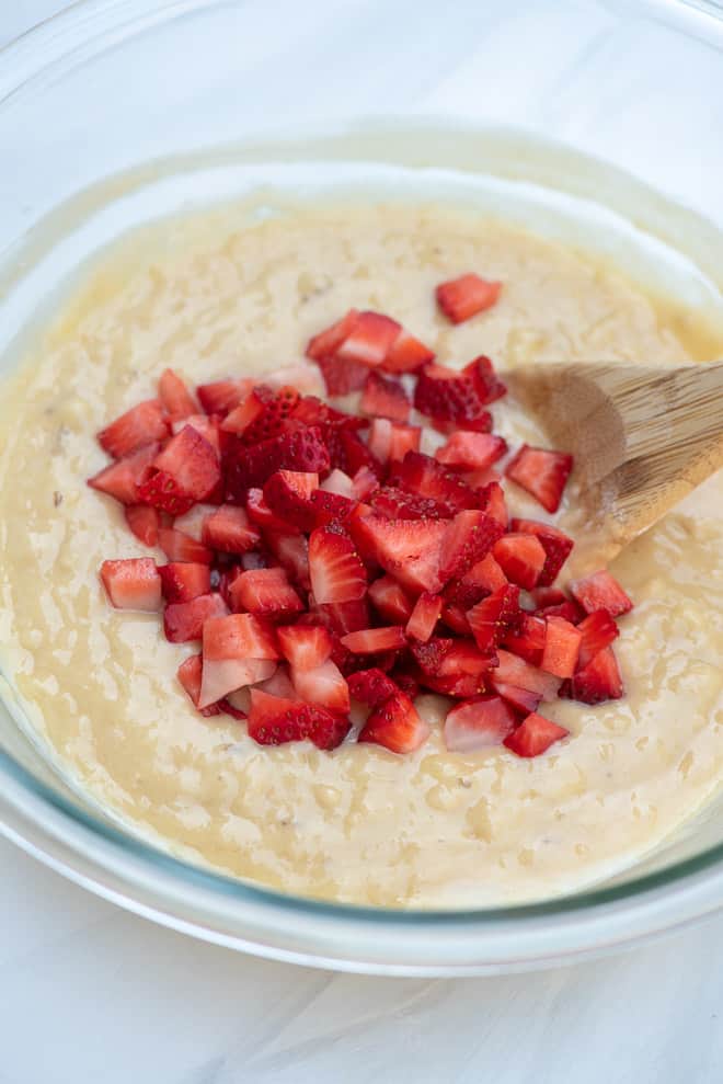 A glass mixing bowl with the bread batter and chopped fresh strawberries on top.