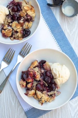 Two white bowls with ice cream and cherry cobbler.