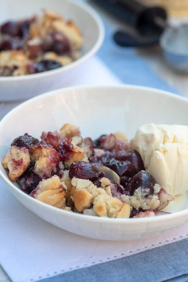 A close up image of Cherry Cobbler in a white bowl with a scoop of vanilla ice cream.