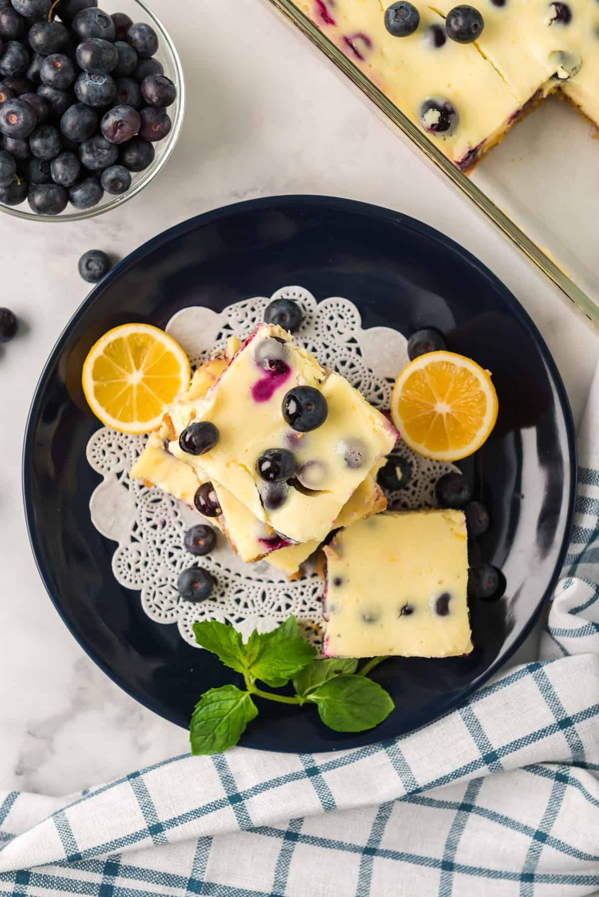 An over the top image of Lemon Blueberry Cheesecake Bars stacked on a black plate.