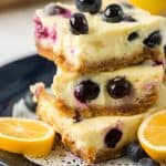 Cheesecake bars with blueberries stacked on a plate.