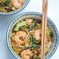 A bowl with shrimp and noodles with chopsticks lying over the top.