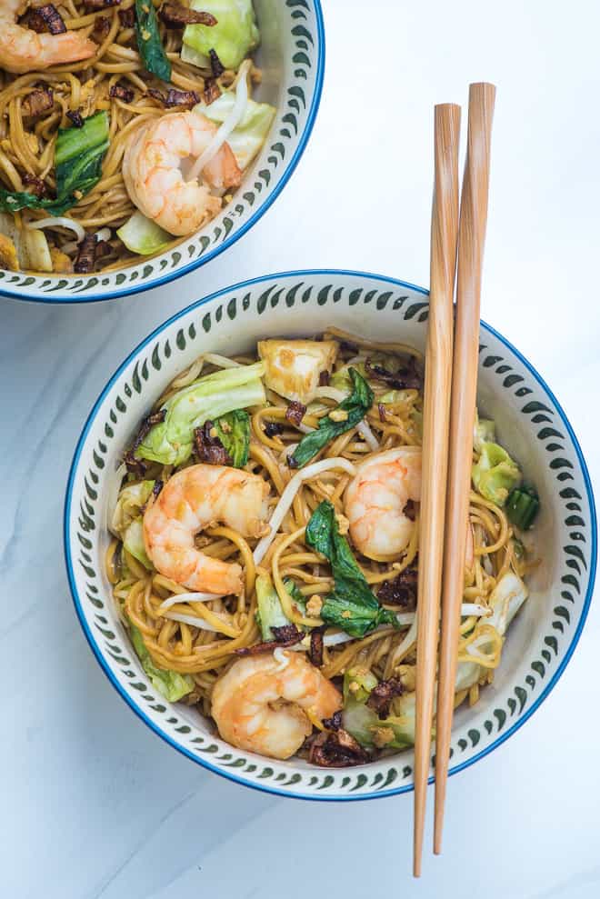 A bowl with shrimp and noodles with chopsticks lying over the top.