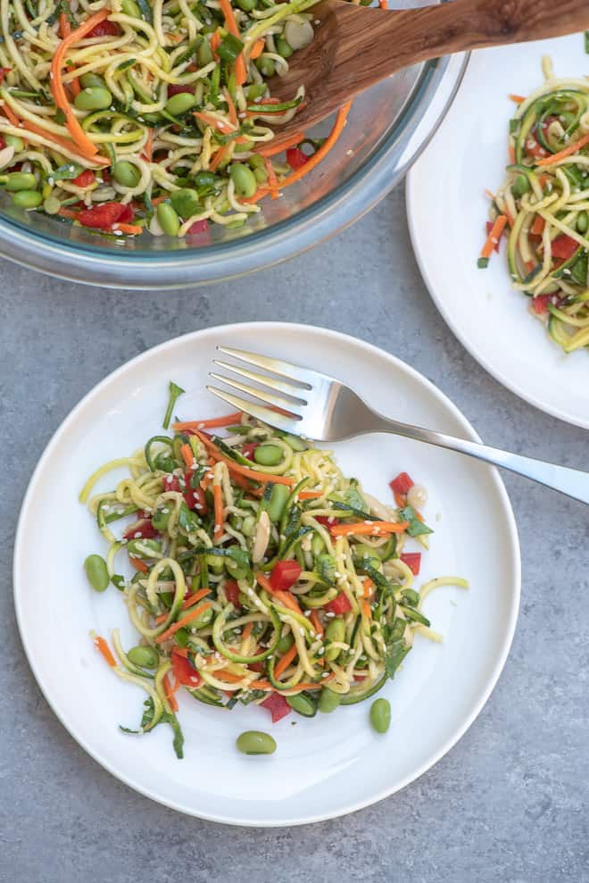 Asian Zucchini Noodle Salad on a white plate with a fork with the serving bowl in the background.