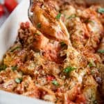 A spoon lifts a stuffed shell from a casserole dish.