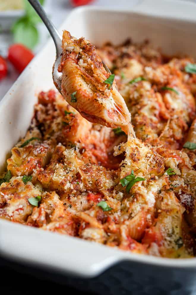 A spoon lifts a stuffed shell from a casserole dish.