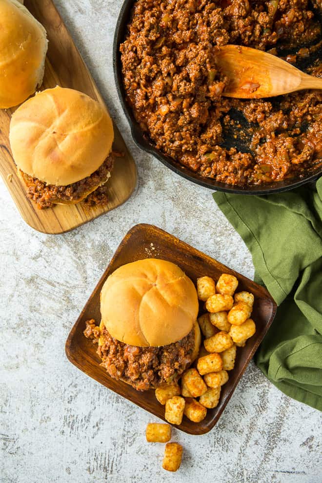 An overhead shot of a Cajun Sloppy Joe on a serving plate with tater tots with the skillet behind it.