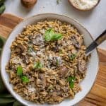 An over the top shot of orzo with mushrooms in a white bowl with a spoon.