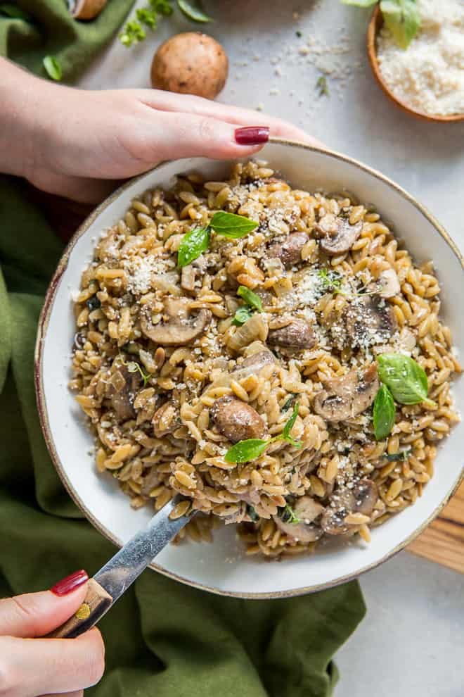 A person holding a bowl filled with orzo and mushrooms.