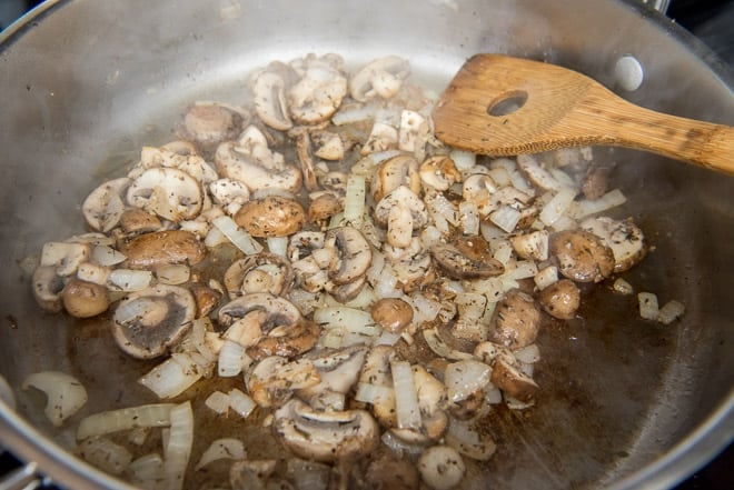 Chopped mushrooms, onions, and garlic cooking in melted butter in a saute pan.