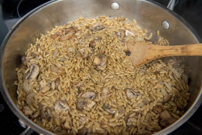 Chicken broth has been added to the orzo and then the mushrooms and onions go back in the pan.
