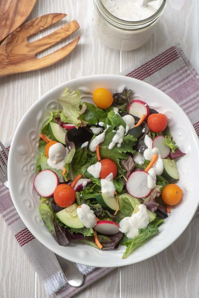A salad in a white bowl with Ranch dressing on top.