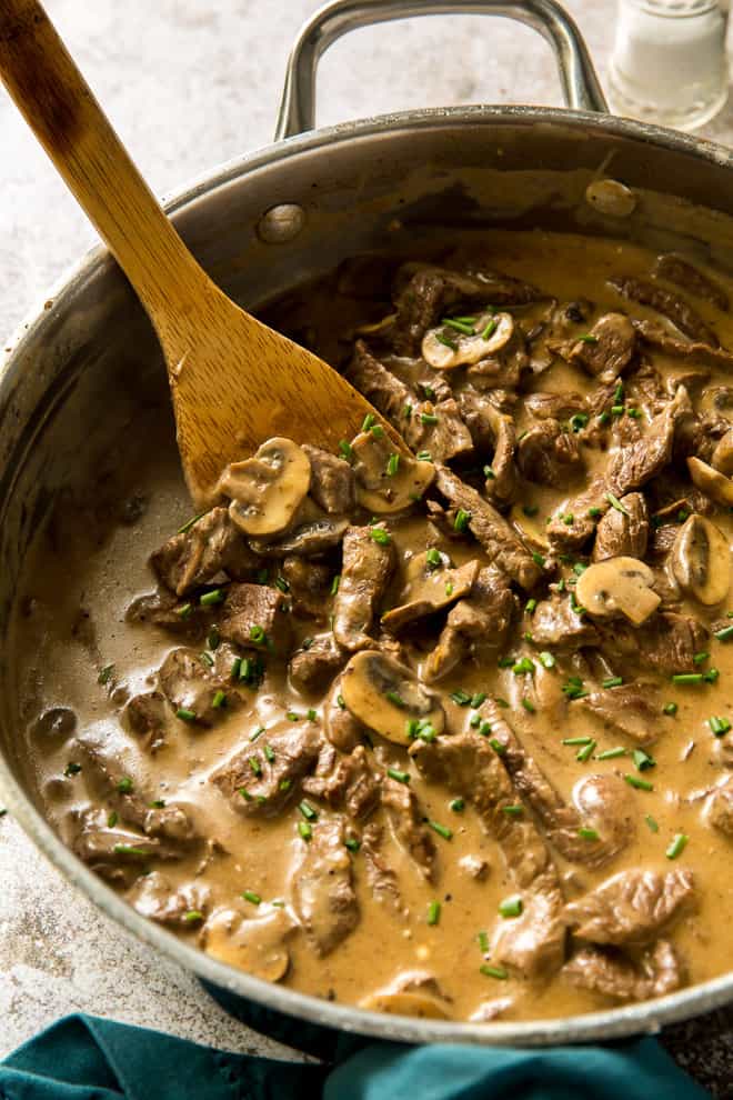 A close up of Beef Stroganoff in a pan with a wooden spoon.