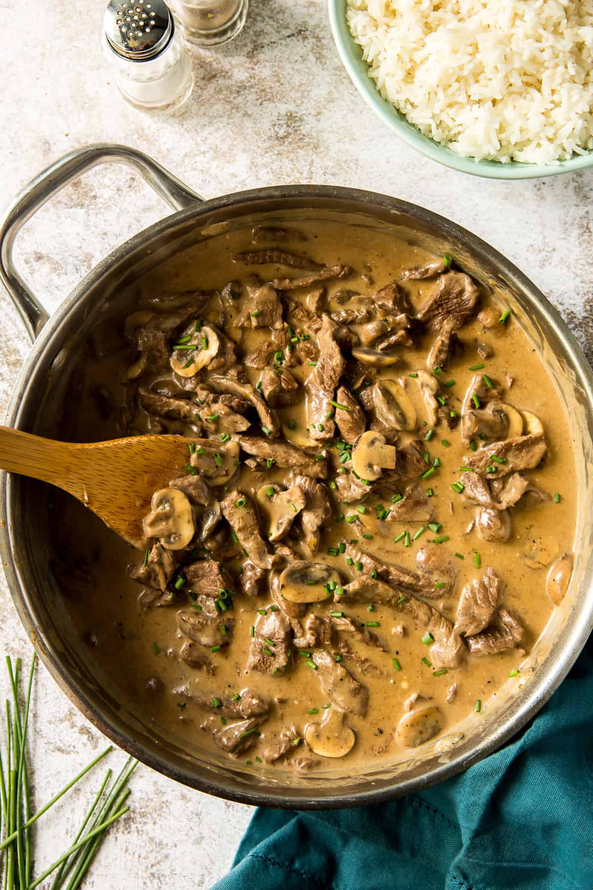 A top down shot of beef stroganoff in a creamy mushroom sauce in a skillet with a wooden spoon.