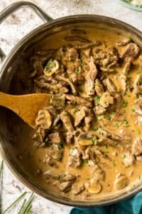 A top down shot of a skillet full of beef stroganoff being stirred with a wooden spoon.