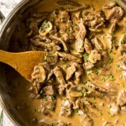 A top down shot of a skillet full of beef stroganoff being stirred with a wooden spoon.