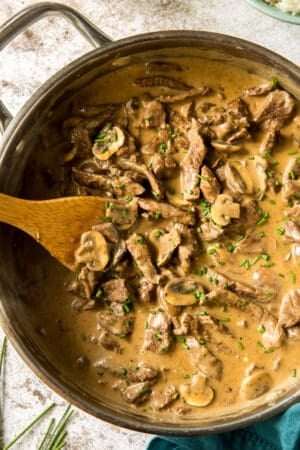 A top down shot of a skillet full of beef stroganoff being stirred with a wooden spoon.