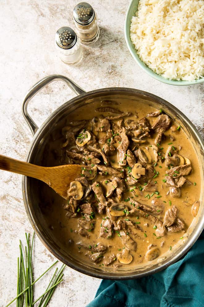 Beef Stroganoof in a pan with a bowl of rice and salt and pepper shakers behind it.