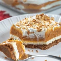 A sliced of layered pumpkin dessert with a fork on a white plate.