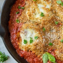 A closeup of a skillet filled with tomato sauce and chicken parmesan.