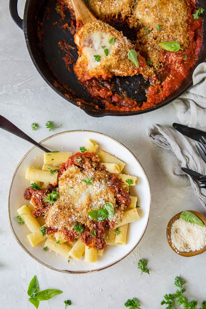 An overhead shot of a skillet full of Chicken Parmesan and a white serving bowl.