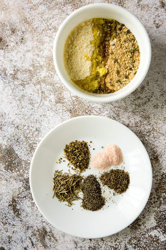 A bowl filled with dried herbs and a second bowl filled with panko break crumbs, Parmesan cheese, and olive oil.