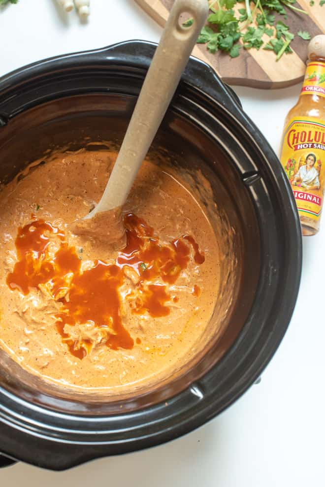 Chicken Enchilada Dip in a slow cooker with hot sauce drizzled over the top.