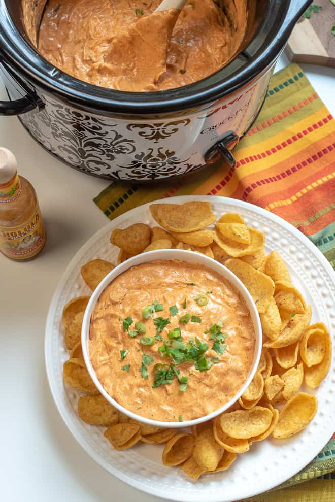 Slow Cooker Chicken Enchilada Dip shot from over the top in a Crock Pot and in a white serving bowl garnished with green onion and cilantro.