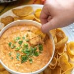 A hand dips a chip into a bowl of chicken enchilada dip.