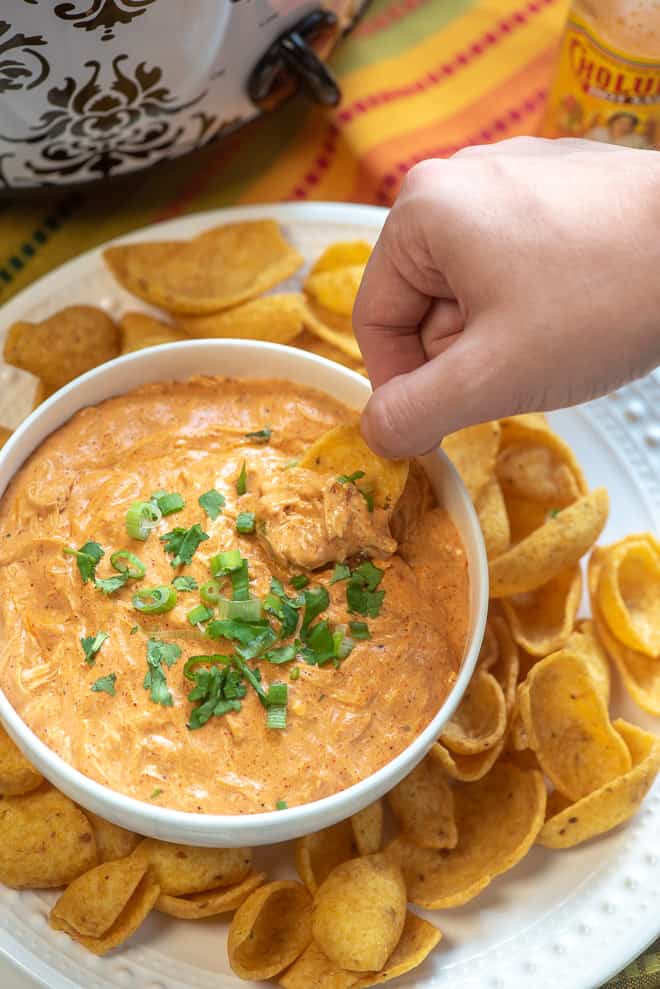 A hand dips a chip into a bowl of chicken enchilada dip.