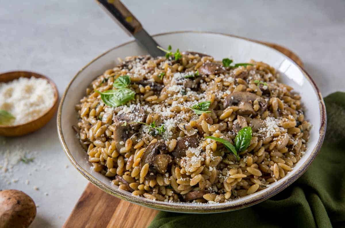 Orzo with mushrooms in a white bowl with a spoon.
