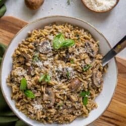 Orzo with mushrooms in a white bowl with a spoon.