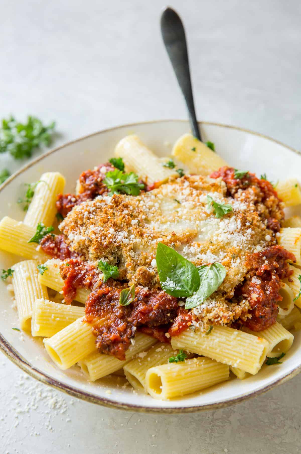 Chicken parmesan over pasta in a white bowl with a fork resting in it.