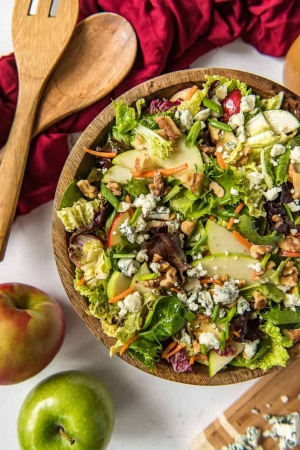 A large wooden bowl filled with salad with apples and cabbage.