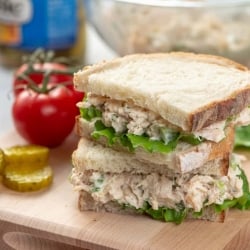 A chicken salad sandwich cut in half and stacked on a cutting board.
