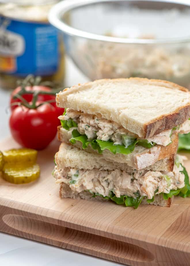 A chicken salad sandwich cut in half and stacked on a cutting board.