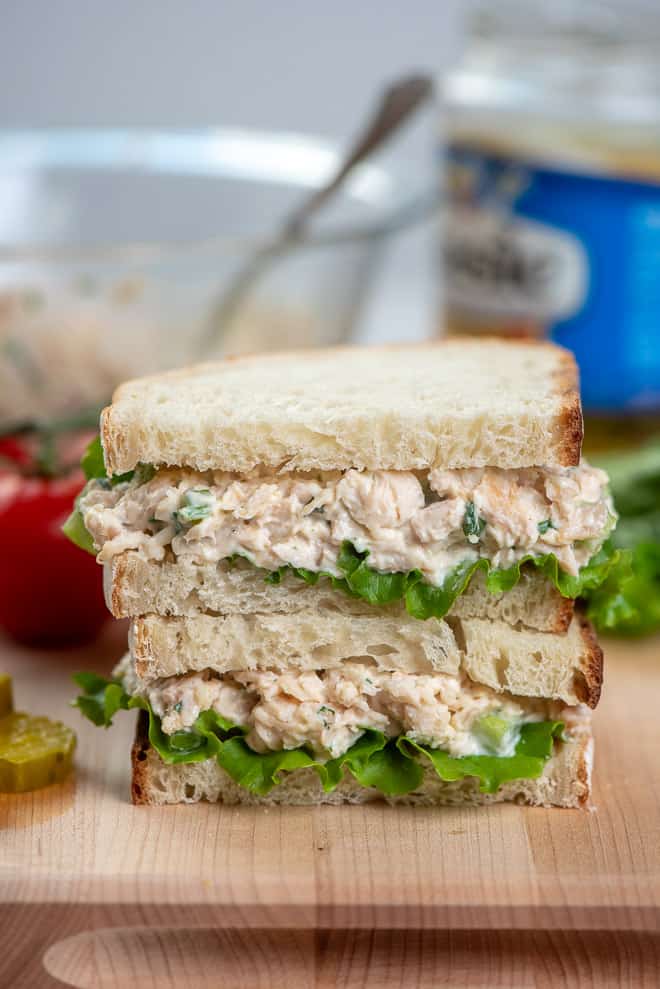 A close up image of a chicken salad sandwich cut in half and stacked on a cutting board.