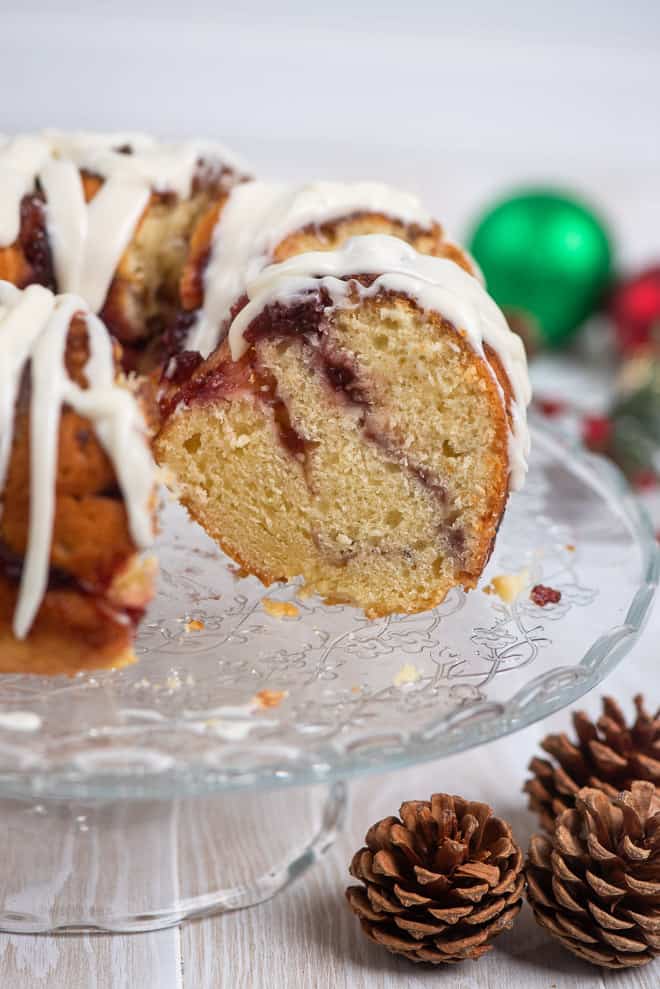 Cranberry Swirl Bundt Cake on a glass pedestal serving plate with pine cones and Christmas ornaments placed around it.